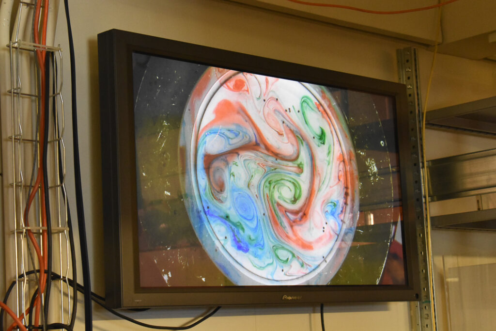 A screen showing a rotating tank filled with a clear fluid mixing blue, green and red dyes.